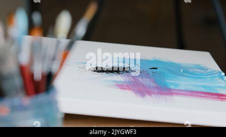 Gros plan noir foncé taches de peinture sur la toile avec rose et bleu image femelle main tenant la main pinceaux de peinture dessine la texture crée Banque D'Images