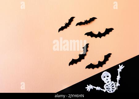 Composition de chauves-souris noires sur fond orange et d'un squelette blanc tricoté sur fond noir. Concept Halloween. Banque D'Images