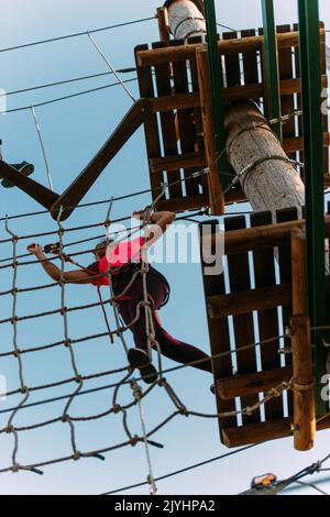 Femme accrochée au mur de cordes essayant de terminer le parcours dans le parc d'aventure Banque D'Images