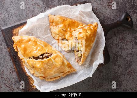 Tarte cuite au four et au cornouailles, garée de viande et de pommes de terre, sur le papier en bois. Vue horizontale du dessus Banque D'Images