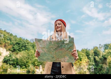 Bonne femme blonde tenant et regardant la carte topographique papier, touriste dans le fond de la forêt en voyage sauvage randonnée pendant les vacances. Banque D'Images