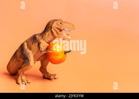 Jouet dinosaure Tyrannosaurus tenant le potiron dans ses pattes isolées sur fond orange carte de vœux de vacances Joyeux jour d'Halloween, Hello Autumn Creative Banque D'Images