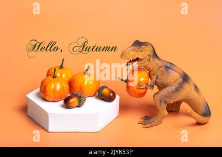 Jouet dinosaure Tyrannosaurus tenant le potiron dans ses pattes, sur le podium blanc isolé sur fond orange carte de voeux de vacances Joyeux jour d'Halloween, Bonjour Banque D'Images