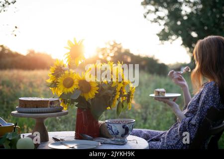 elle est assise dans le jardin et mange une tarte. tarte, vase avec tournesol et pommes sur une table Banque D'Images