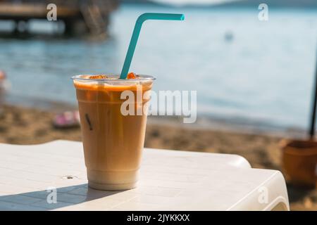 Café glacé en verre plastique sur la plage. Banque D'Images