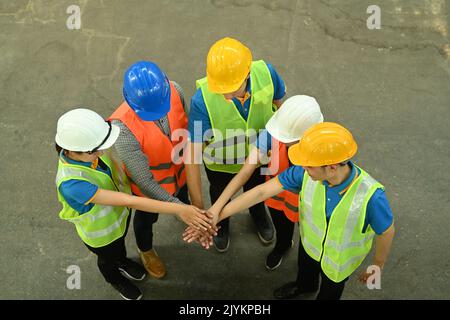 Vue en hauteur des employés de l'entrepôt en casque et en gilets réfléchissants pour empiler les mains ensemble. Logistique, occupation de magasin Banque D'Images