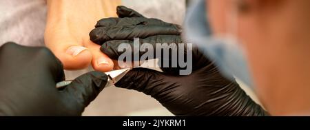 Pédicure professionnelle. Pédicure maître portant des gants en latex coupe les ongles du pied féminin dans le salon de beauté, gros plan Banque D'Images