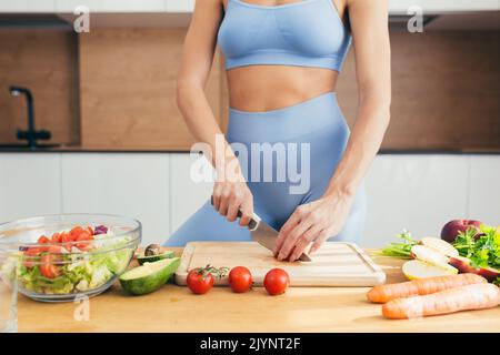 Gros plan photo, partie du corps, mains de la jeune femme de forme physique coupant des légumes frais sur la salade de cuisine à la maison Banque D'Images