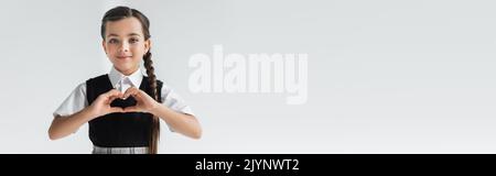 portrait de bonne écolière montrant le cœur avec les mains isolées sur gris, bannière, image de stock Banque D'Images