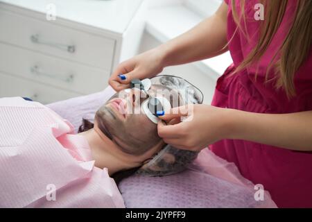 une femme porte des lunettes de protection sur des tampons de coton au-dessus de ses yeux pendant la procédure d'écaillage au carbone. Banque D'Images