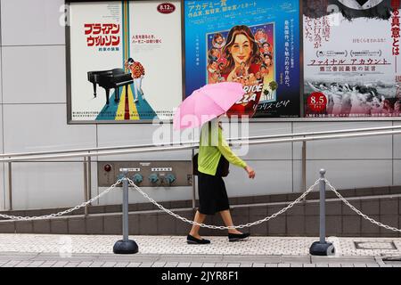 TOKYO, JAPON - 1 septembre 2022 : un piéton tenant un parasol passe devant des affiches de cinéma sur un cinéma Toho dans la région de Hibiya à Tokyo. Banque D'Images