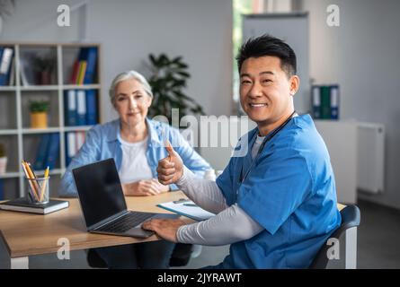 Gai adulte asiatique homme médecin montrant le pouce vers le haut signe avec la main et la consultation femme âgée patient Banque D'Images