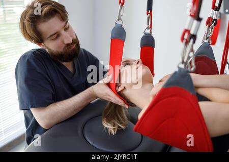 Un physiothérapeute aide une patiente subissant une physiothérapie réhabilitative sur un système de corde de suspension. Clinique moderne utilisant la réhabilitatine avancée Banque D'Images