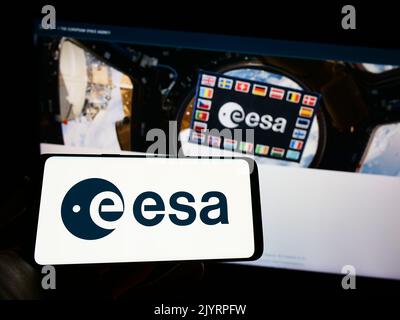 Personne tenant un téléphone portable avec logo de l'Agence spatiale européenne (ESA) Europen sur écran devant la page web. Mise au point sur l'affichage du téléphone. Banque D'Images