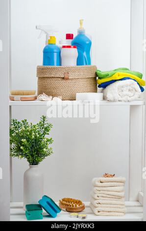 Panier en jute tricoté à la main avec un couvercle avec des détergents et des serviettes dans la salle de bains sur un rack en bois blanc. Banque D'Images