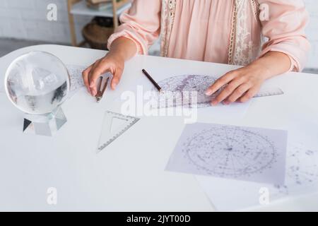 vue rognée de l'astrologue en dessinant la carte céleste à la maison Banque D'Images