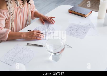 vue partielle de jeunes astrologues dessinant des cartes cosmiques près du cristal magique Banque D'Images