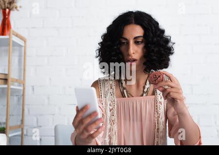 brunette fortune teller regardant le téléphone mobile et tenant la rune d'argile Banque D'Images