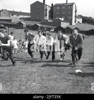 1965, hommes adultes historiques participant à une compétition de course dans un champ dans un domaine d'habitation à North Queensferry, Fife, Écosse, Royaume-Uni, dans le cadre de la journée de gala de North Queensferry, une journée d'activités communautaires pour les résidents. Banque D'Images