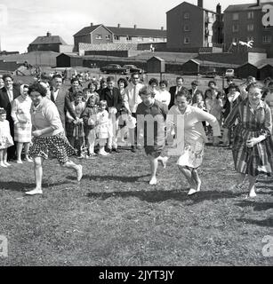 1965, historique, les femmes prenant part à une compétition de course, deux dans les pieds de bareft, sur l'herbe dans un champ dans un domaine de logement à North Queensferry, Edimbourg, Ecosse, Royaume-Uni, dans le cadre de la journée de gala de North Queensferry. Banque D'Images