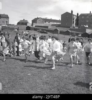 1965, historique, les femmes prenant part à une compétition de course, plusieurs dans les pieds de bareft, sur l'herbe dans un champ dans un domaine d'habitation à North Queensferry, Fife, Écosse, Royaume-Uni, dans le cadre de la journée de gala de North Queensferry. Banque D'Images