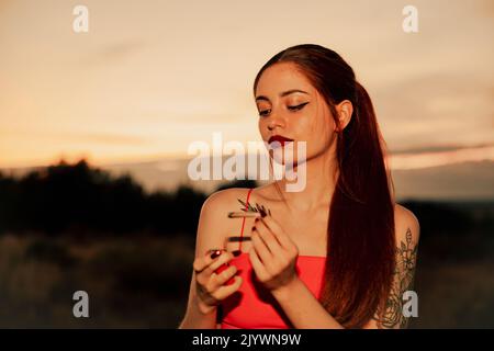 Fille dans une robe rouge fumant un joint de marijuana pendant le coucher du soleil Banque D'Images