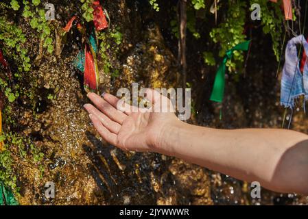 La femme a mis sa main sous la cascade . Des rubans de couleur sont attachés à la cascade pour Bonne chance. Banque D'Images