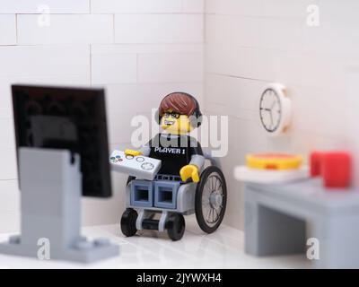 Tambov, Fédération de Russie - 6 septembre 2022 Un jeu vidéo Lego Guy minifigure en fauteuil roulant jouer à un jeu vidéo avec une manette. Banque D'Images