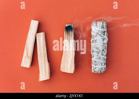 Encens couvants. Sauge blanche et bâtonnets de palo santo dans une rangée sur fond rouge orange. Paquet pour la méditation et la fumigation de salle. Mise au point sélective. Banque D'Images