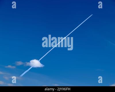 De petits jets à distance créent des pistes de chimie diagonales dans le ciel bleu à travers un petit nuage bas bouffé dans le ciel du Yukon. Banque D'Images