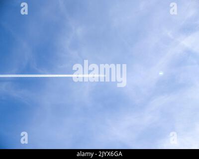 Les petits jets à distance créent des traces chimiques horizontales sur le ciel bleu vers le point d'éclat lumineux de la lentille. Banque D'Images