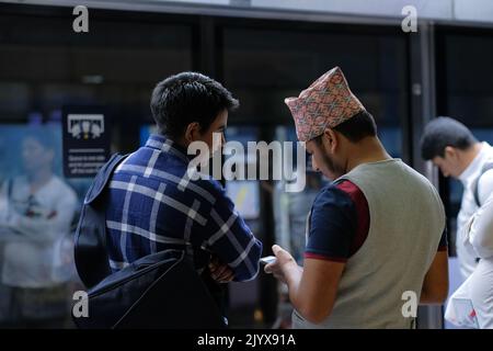 Deux hommes parlent en attendant à une plate-forme de train. Un homme porte un gilet et un chapeau islamique brodé. Un autre mâle a un grand sac noir suspendu. Banque D'Images