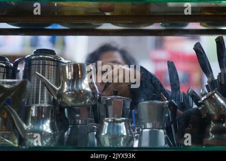 Femme ramasse une petite bouilloire d'argent sur une étagère en verre à l'intérieur d'un magasin dans un souk (marché arabe). L'accent est mis sur la main, du point de vue de l'extérieur de la boutique. Banque D'Images