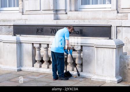 Nouveau concept de balai. Ouvrier balayant des feuilles et des mégots de cigarettes devant le Cabinet Office, 70 Whitehall, Westminster, Londres, Royaume-Uni Banque D'Images