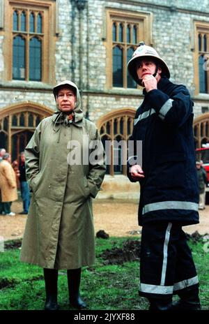 Photo du dossier datée du 21/11/1992 de la reine Elizabeth II inspectant les ruines du château de Windsor avec un pompier. Le discours de la Reine Annus horribilis à Guildhall le 24 novembre 1992, marquant 40 ans sur le trône, suivi d'une année qui avait vu le prince et la princesse de Galles en guerre, le duc et la duchesse de York séparés, la princesse Anne divorcée, Le château de Windsor monta en flammes et la publication du livre d'Andrew Morton : « diana: Her True Story ». En décembre, le prince et la princesse de Galles se sont officiellement séparés. Date de publication : jeudi 8 septembre 2022. Banque D'Images