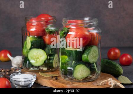 Les concombres et les tomates cerises sont placés dans des pots avec de l'ail, des feuilles de Laurier, du poivre et de l'aneth. Préparation au décapage, étape par étape Banque D'Images