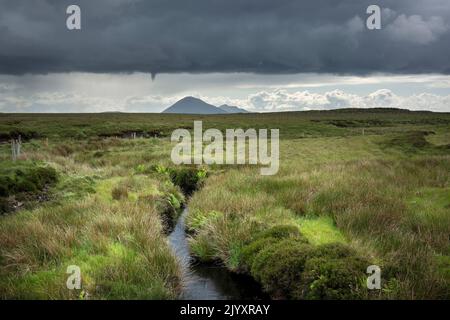 Le vaste paysage tourbé du comté de Mayo en Irlande, avec Slievemore sur l'île d'Achill à l'horizon. Des nuages sombres s'amassent au-dessus du paysage vert Banque D'Images