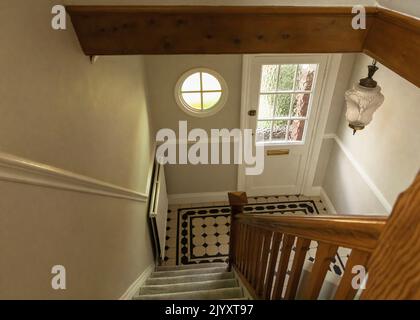 Winsford, Cheshire, Royaume-Uni - 8 juin 2022 - vue sur un escalier au sol carrelé noir et blanc, une fenêtre ronde originale et une porte avant peinte en blanc Banque D'Images
