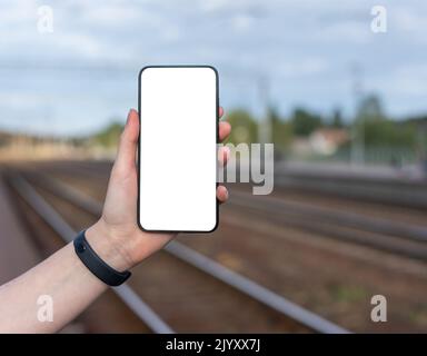 Main tenant le téléphone maquette sur fond de chemin de fer. Application mobile avec horaire de train en ligne, possibilité de réservation, paiement. Modèle de smartphone avec Whi Banque D'Images