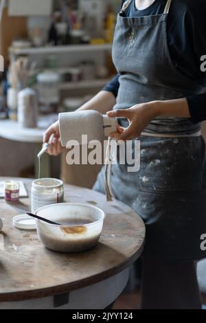 Jeune artisan peint vase avec pinceau après la cuisson et façonnage fait à la main en studio Banque D'Images