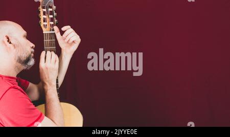 Instrument de musique à cordes. Guitariste masculine charismatique mature. Guy avec barbe tient de la guitare. Homme barbu dans une chemise rouge. Interprète musical de la musique. Banque D'Images