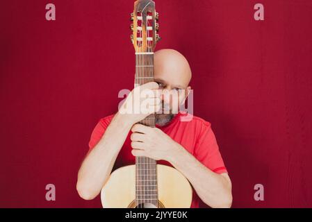 Instrument de musique à cordes. Guitariste masculine charismatique mature. Guy avec barbe tient de la guitare. Homme barbu dans une chemise rouge. Interprète musical de la musique. Banque D'Images