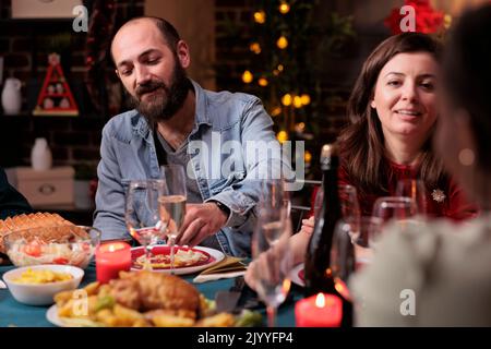 Couple célébrant noël en famille, parlant à table de fête, manger traditionnel repas de vacances d'hiver, boire du vin mousseux. Fête de Noël à la maison, conversation entre femme et mari Banque D'Images