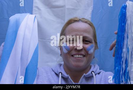 Femme blonde avec un drapeau et un visage peint dans les couleurs de l'Argentine regardant un match de football. Banque D'Images