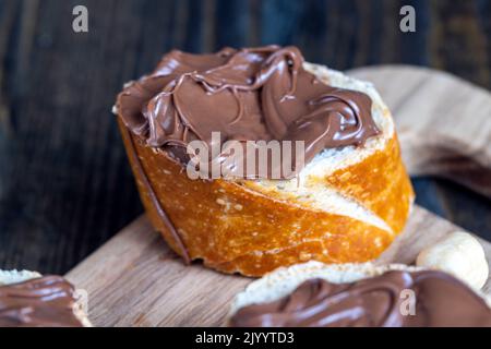 tartiner le beurre de chocolat sur une baguette, le beurre de chocolat doux sur une baguette pendant la préparation d'un simple dessert à la maison Banque D'Images