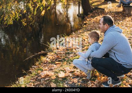 Portrait de famille heureuse : père avec son petit garçon regardant un lac d'automne en vacances. Week-end dans le parc d'automne. Coucher de soleil d'été. Heureux Banque D'Images