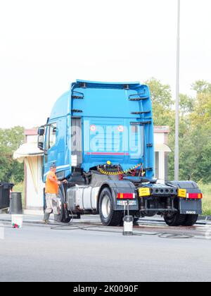 Homme pulvérisant l'extérieur d'un semi-camion bleu à l'aide d'un équipement libre-service au lavage de voiture. Banque D'Images