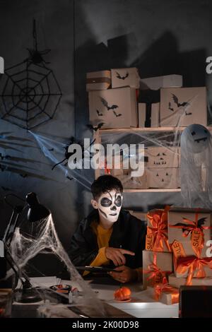 Livraison. Un homme avec un maquillage de crâne se trouve dans son bureau à la maison parmi des boîtes de toiles d'araignée, gardant la trace des boîtes à expédier. Le concept d'un grand Banque D'Images