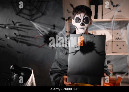 Chute propriétaire d'affaires d'expédition porte le crâne d'argile blanc, maquillage professionnel dans le bureau à la maison. Tenant un sac noir. Bureau décoré Prizdnichny. Halloween Banque D'Images