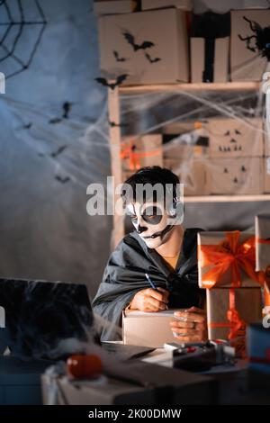 Chute propriétaire d'affaires d'expédition porte le crâne d'argile blanc, maquillage professionnel dans le bureau à la maison. Accepte une commande sur le site écrit l'adresse sur la boîte Banque D'Images
